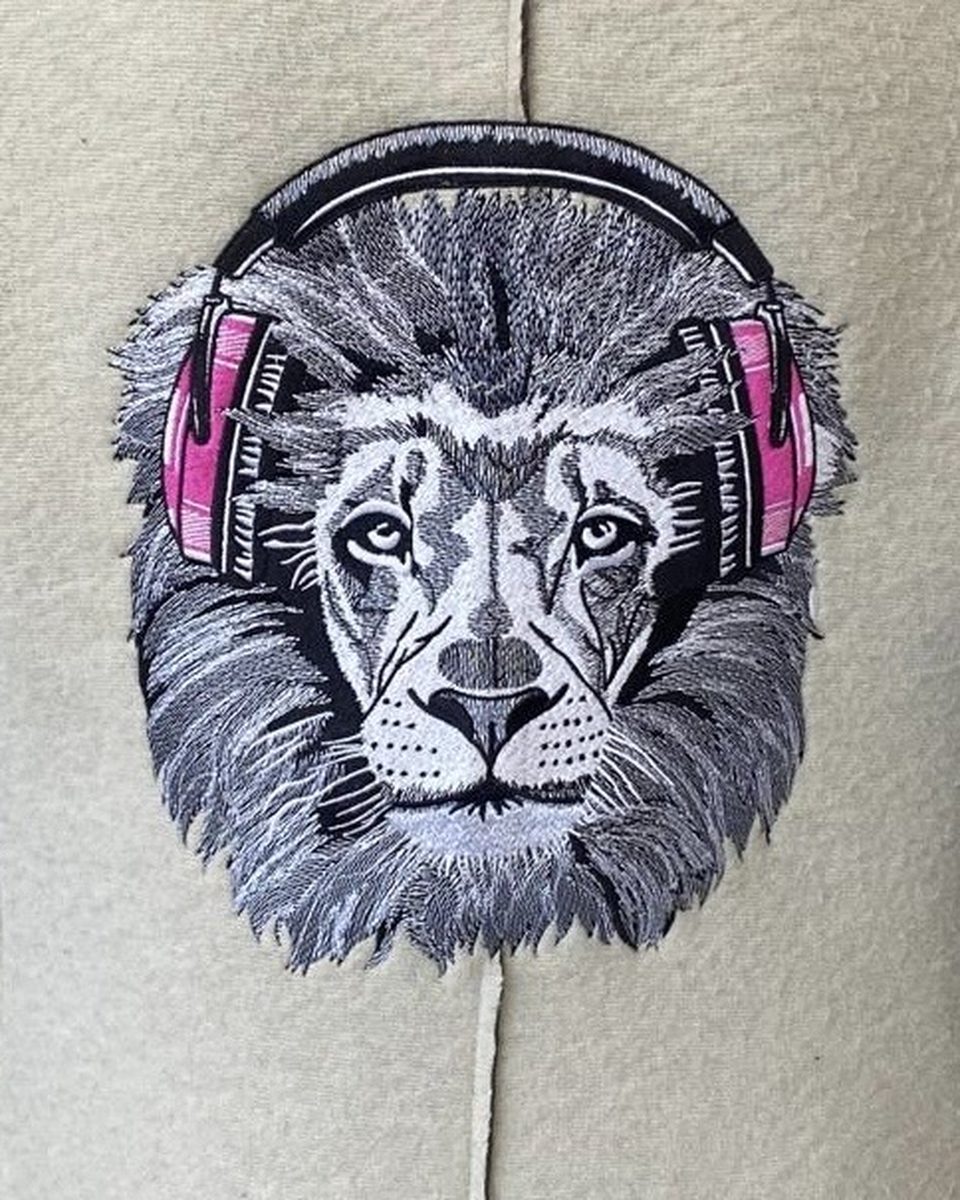 Tête de lion brodée en noir et blanc avec un casque audio rose, sur veste en laine